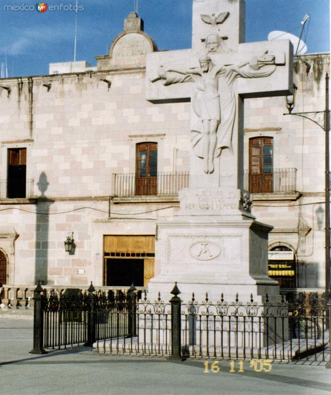 Cruz de cantera en el atrio de la Basílica y al fondo el Palacio Municipal. 2005